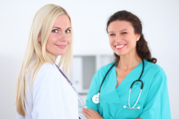 Fototapeta premium Beautiful young smiling female doctor standing at hospital with doctor on the background. Medical concept.