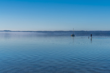 Starnberger See mit Morgennebel, Segelyacht und Stehpaddler