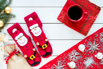 knitted Christmas Stockings as Santa Claus on white painted wood background with Christmas tree and decorations. Red tablecloth with silver Christmas tree decorations. Top view, free space for text.