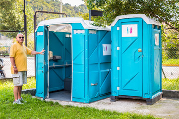 Blue portable toilet cabins in the park with a man of entrance.  - obrazy, fototapety, plakaty