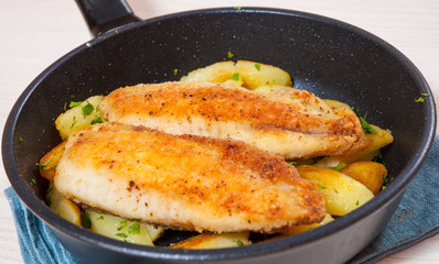 Fried fish fillet and potatoes in a frying pan