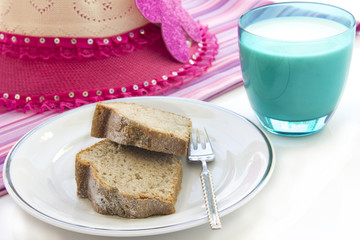 a glass of milk with slice homemade cake and pink hat in the morning
