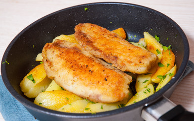 Fried fish fillet and potatoes in a frying pan