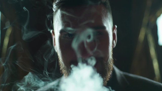 close-up of a bearded man in suit smoking electronic cigarette
