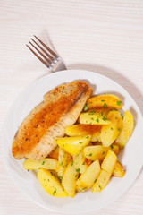 Fried fish fillet and potatoes in a plate