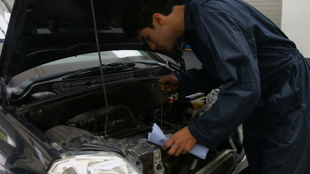 Handsome mechanic checking oil in a car engine