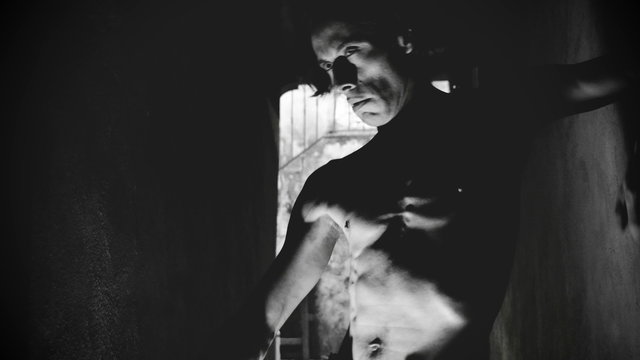 Drunk and high skinny shirtless man dancing in narrow stone alley way close up in black and white.