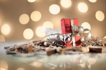 Christmas decoration with red gift box and wooden elements. Lights in background. Shallow depth of field. 