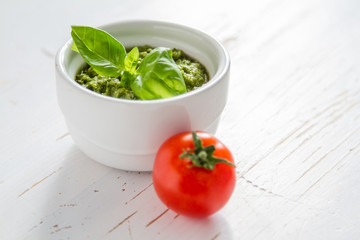 Pesto sauce in bowl, white wood background