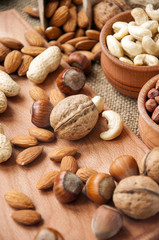 Almonds, cashew, walnuts and hazelnuts in wooden bowls on wooden board and burlap, sack background