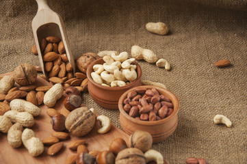Almonds, cashew, walnuts and hazelnuts in wooden bowls on wooden board and burlap, sack background