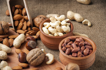 Almonds, cashew, walnuts and hazelnuts in wooden bowls on wooden board and burlap, sack background