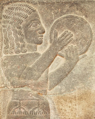 Historical Assyrian relief of musician with drum playing music.