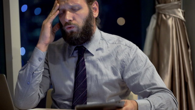 Young businessman having headache during work with laptop and tablet in office 
