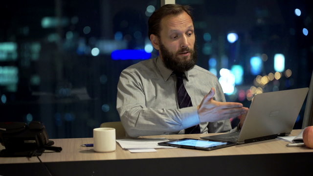 Unhappy businessman with laptop and tablet talking bad news in office at night
