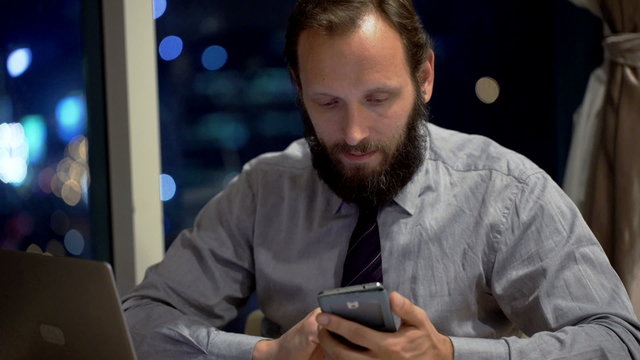 Young businessman using smartphone by desk in office at night
