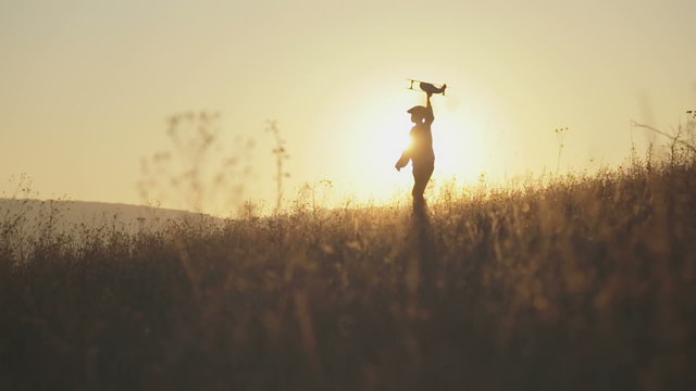 Boy with the airplane in hand runs on the background of sunset