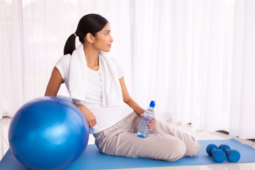 thoughtful indian woman sitting on exercising mat