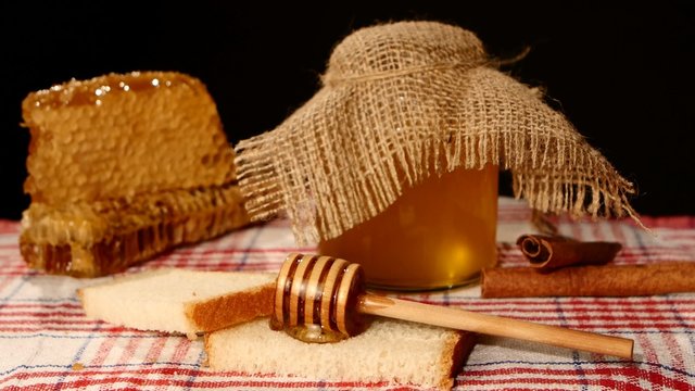 Honey spoon dripper, jar with stick pouring over toast bread, honeycomb on black