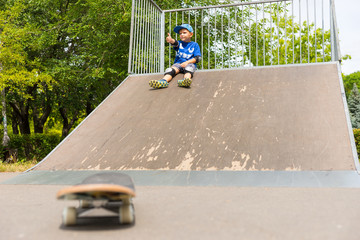 Young Boy Sitting on Top of Ramp in Skate Park