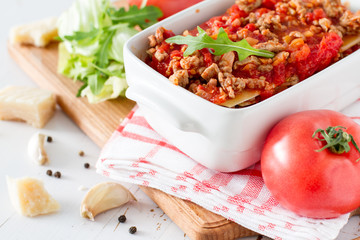 Raw lasagna and ingredients, white wood background