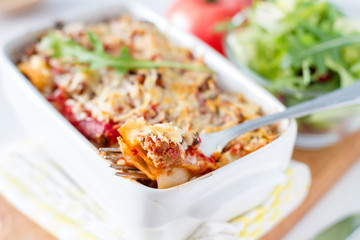 Lasagna served in white bowl with salad