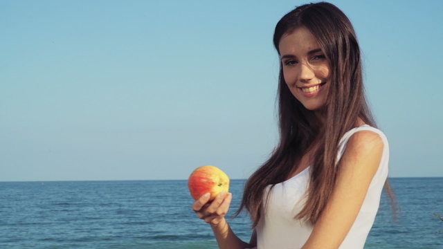 smiling young female holding an apple with the sea in the background