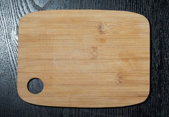 Modern light wooden cutting board with ring hole on a black tabl