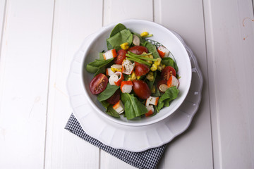 spinach salad with cherry tomatoes and corn in bowl, white wooden table