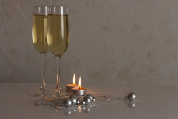 Greeting card template made of two glasses of champagne with two candles, silver christmas balls and silver string of beads with copy space