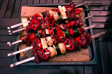 Caucasian shashlik skewers filled with raw meat and vegetables on an oven plate on a rainy summer day outdoors.