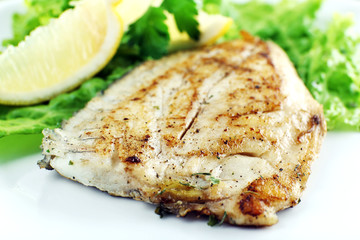 Dish of fish fillet with lettuce and lemon on plate close up