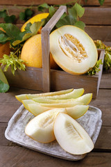 Ripe melons with green leaves in crate on table close up
