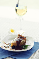 Delicious cake under chocolate glaze with blackberry  and wine glass on blue serviette