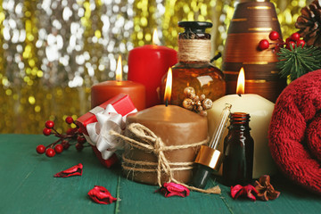 Composition of alight candles, towel and aroma oil on green wooden table against sparkle background