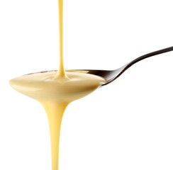 Condensed milk pouring from a spoon, isolated on white