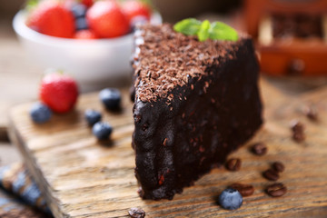 Chocolate cake with chocolate cream and fresh berries on tray, on wooden background