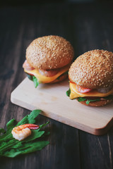 burger with shrimp , cheese and arugula on a wooden stand