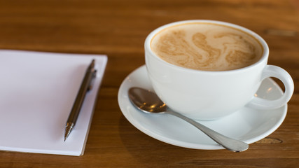 Hot latte art coffee cup on wooden table and note book, vintage