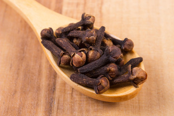 Heap of cloves with wooden spoon on table, seasoning for cooking