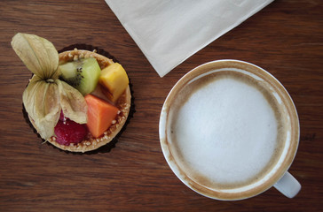 Cup of hot coffee and fruit tart and tissue paper on table