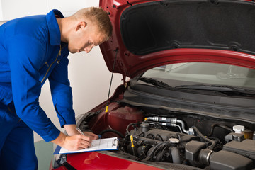 Mechanic Standing Near Car Writing On Clipboard