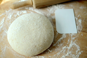 Whole wheat pizza dough ball with a rolling pin and a scraper on a floured working surface - obrazy, fototapety, plakaty