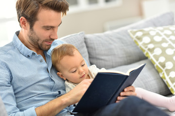 Father and child reading book in sofa