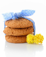 Stack of three homemade oatmeal cookies tied with blue ribbon in small white polka dots and tiny yellow flowers, isolated on white background