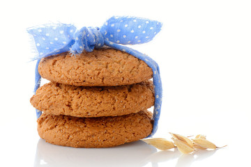 Stack of three homemade oatmeal cookies tied with blue ribbon in small white polka dots and ear of oats, isolated on white background