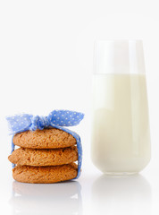 Stack of three homemade oatmeal cookies tied with blue ribbon in small white polka dots and glass of milk, isolated on white background