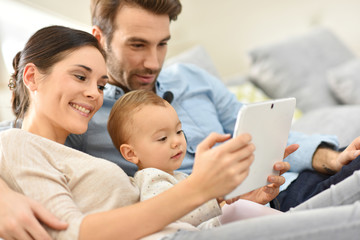 Parents with baby girl in sofa using digital tablet