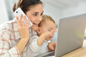 Busy young businesswoman working on laptop, baby on lap