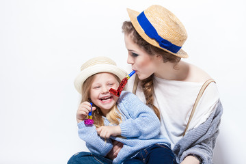 Gorgeous young mother blowing on a party favor while hugging daughter